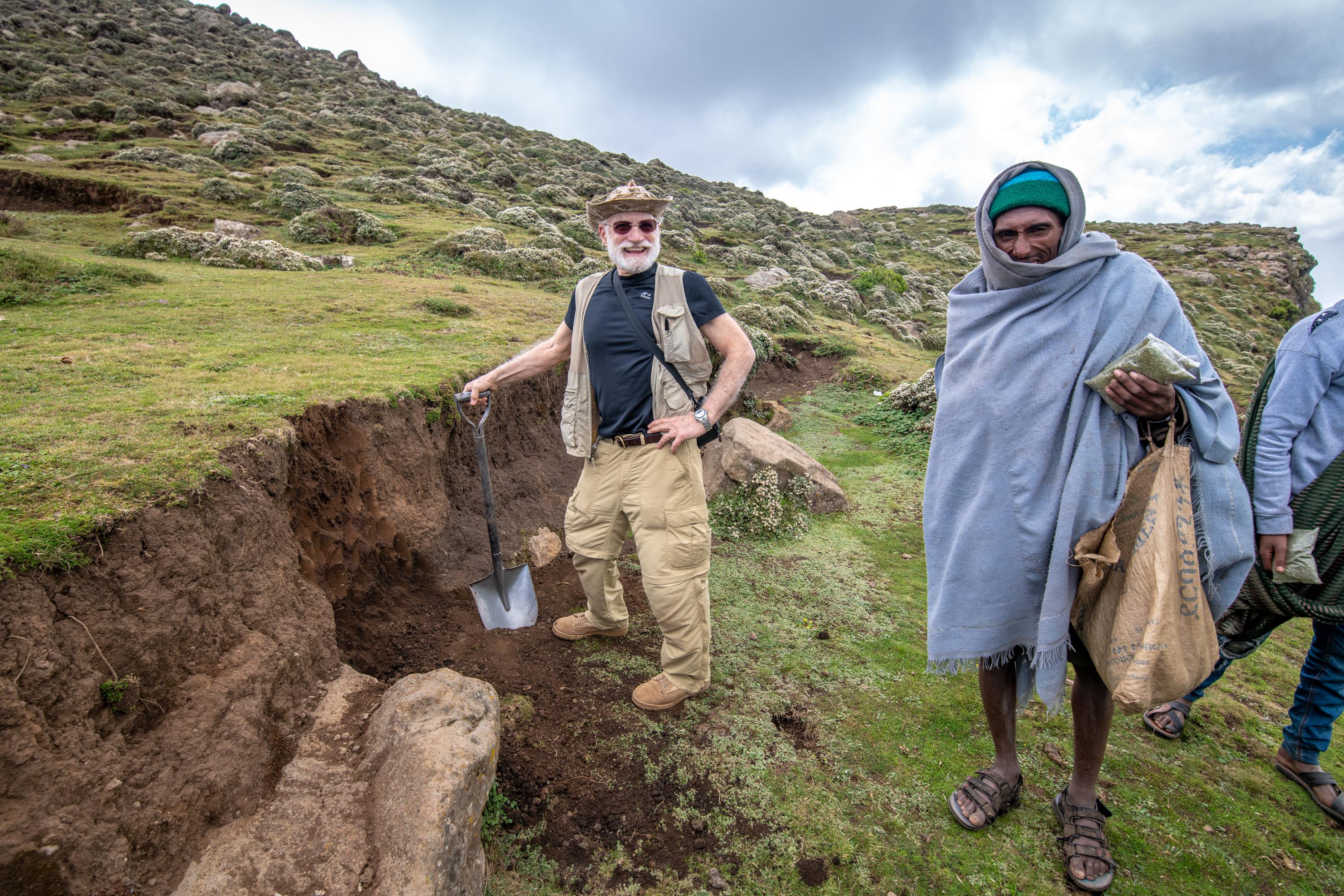 Man digging in countryside as interested bystanders watch