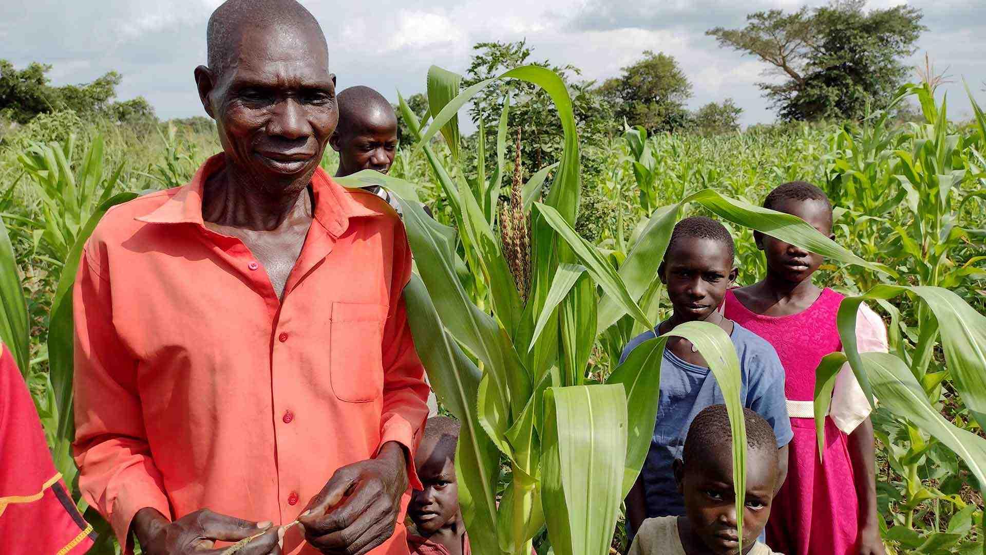 Farmer stands in a field of crops with his family.