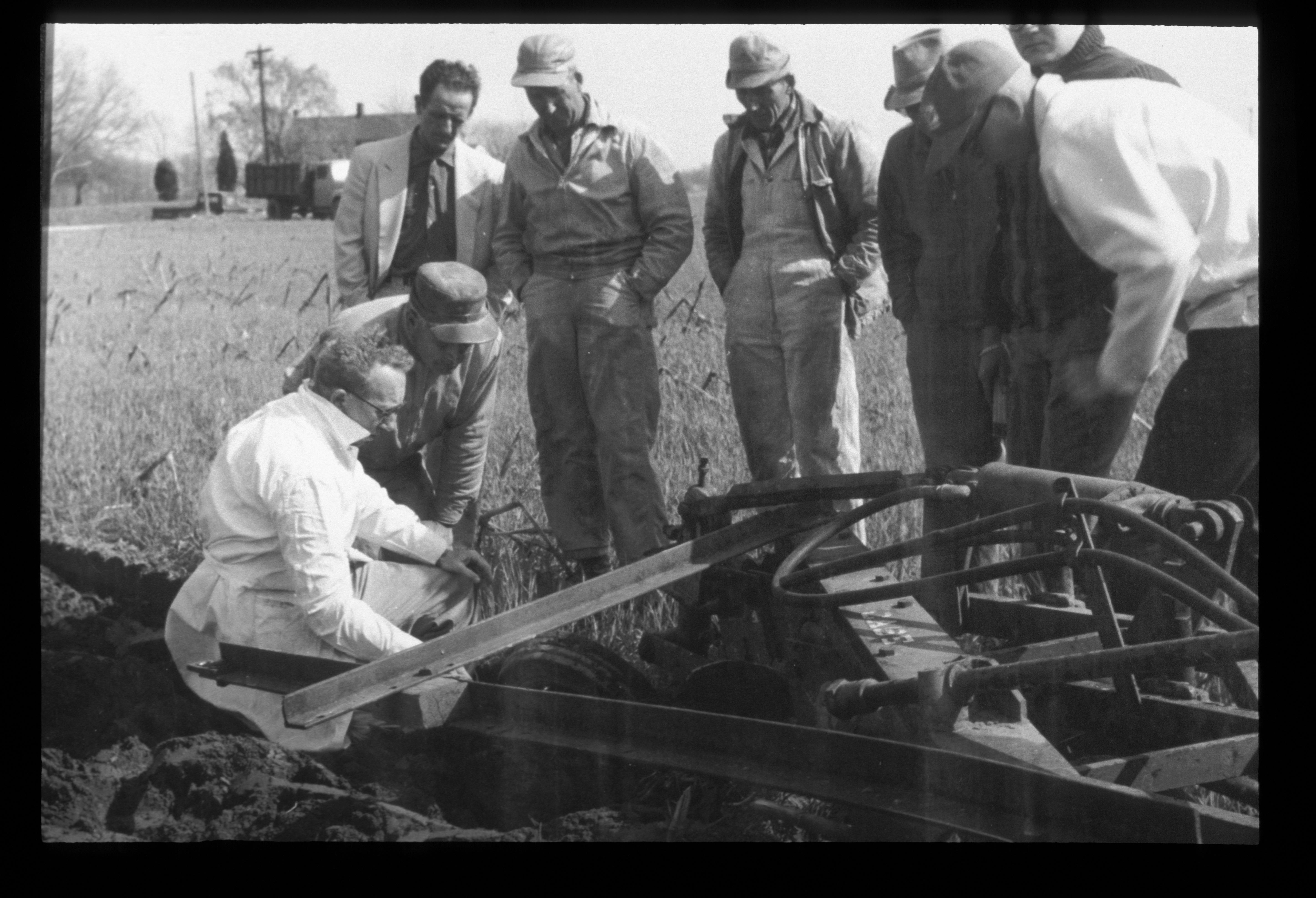 Historic image of men standing and kneeling around an agricultural tool