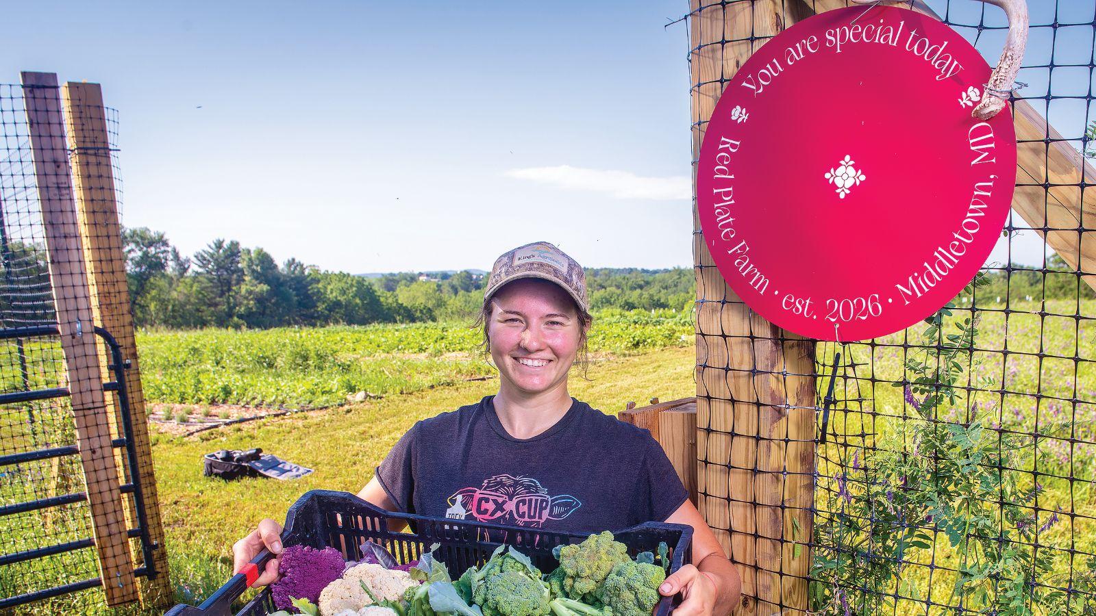 Erin Hyman holding up vegetables in front of a farm field