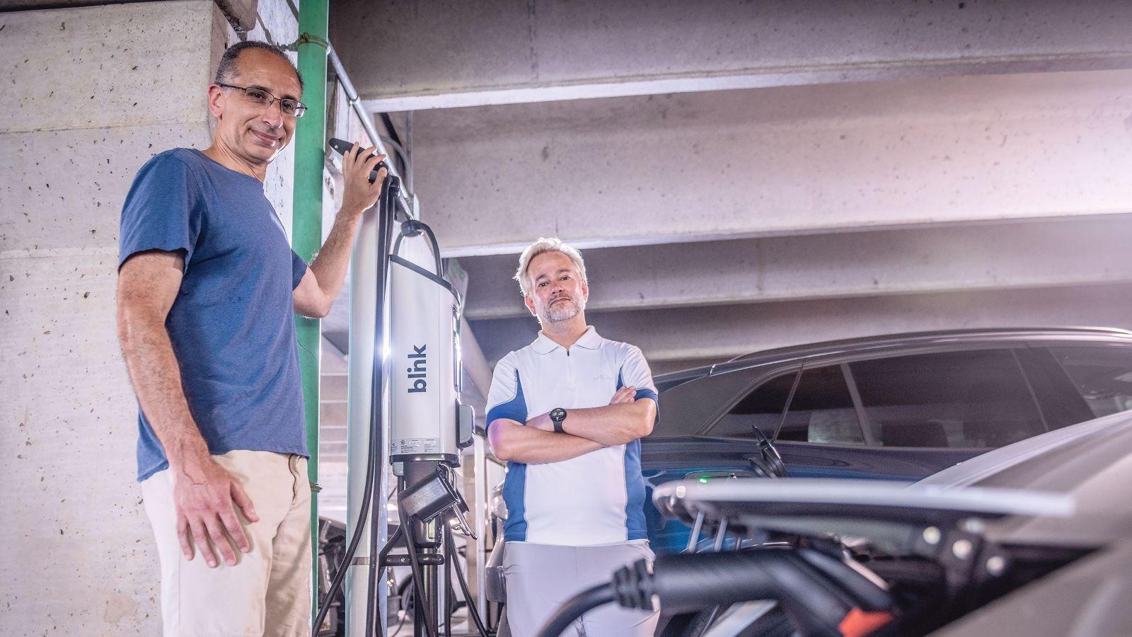 AREC professors standing by electric vehicles in a parking garage 