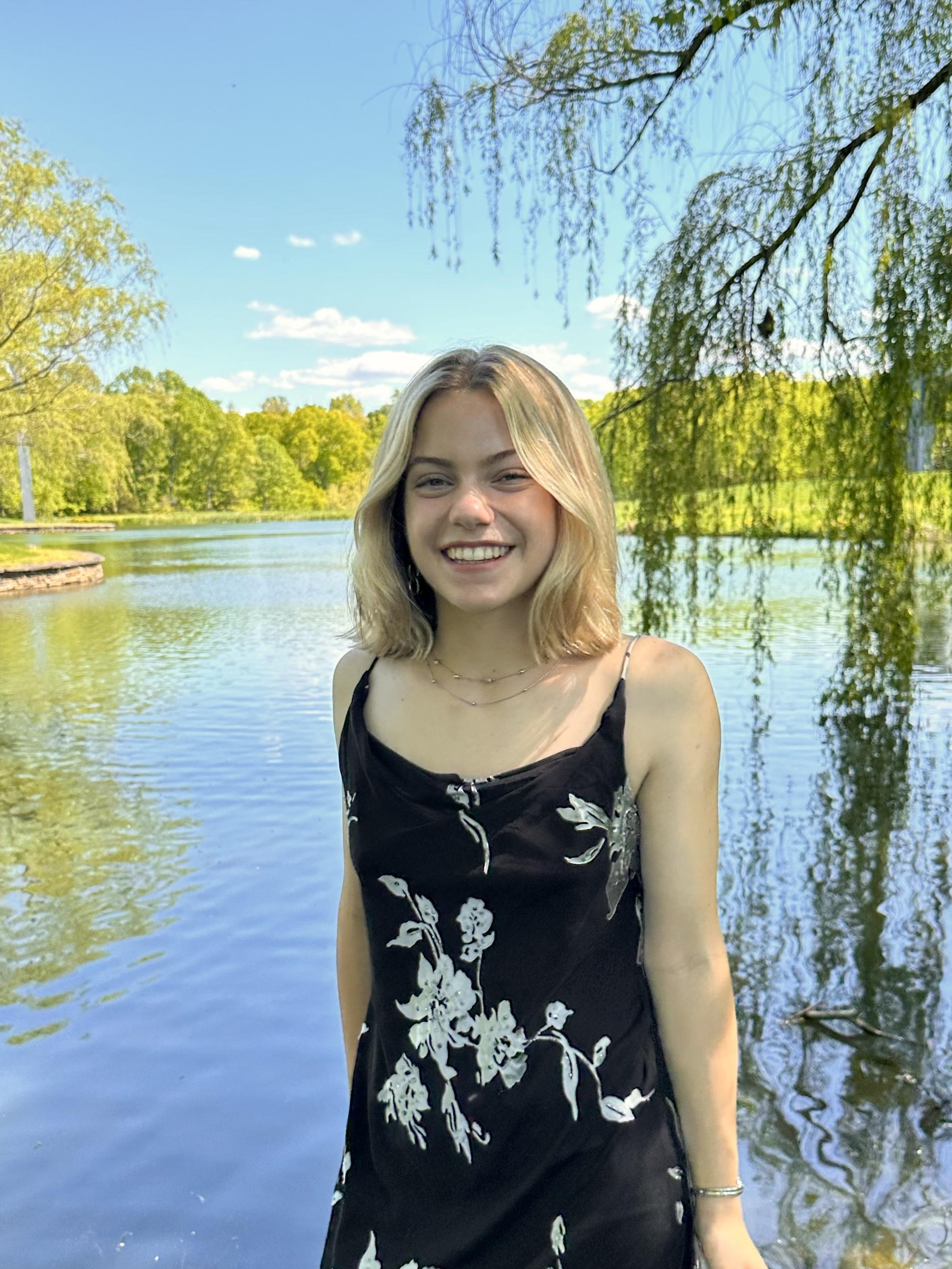 Happy student standing in front of a picturesque lake and blue sky