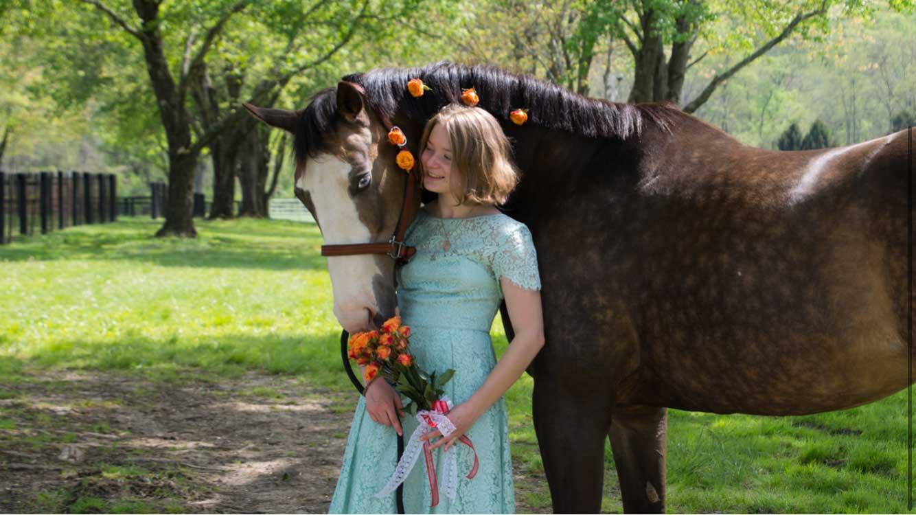 Formally dressed student posing with rose-studded horse.