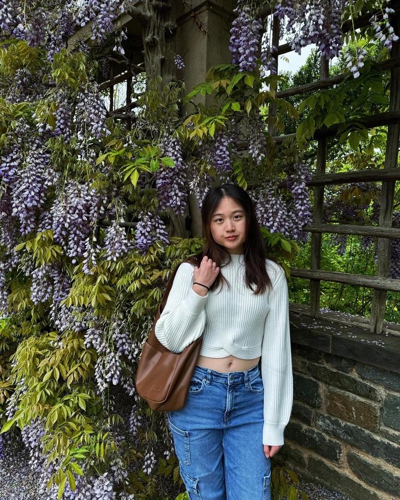 Demure student standing next to purple flowering Wisteria.