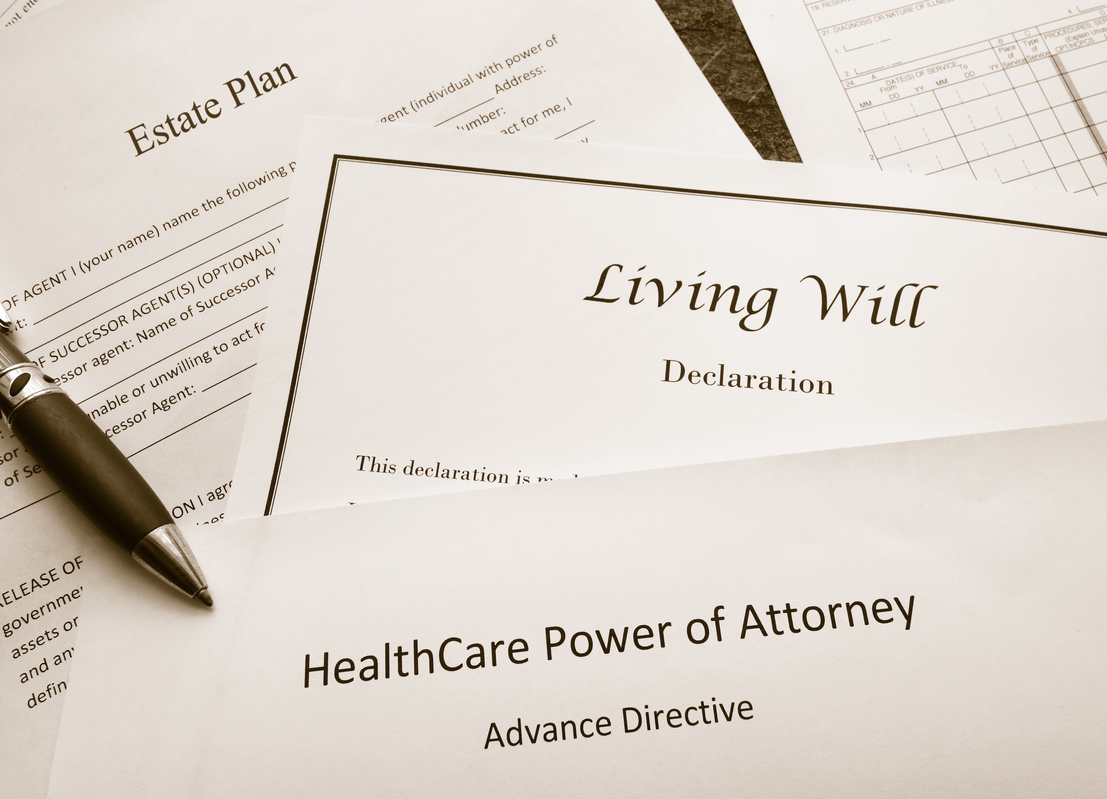 Image of documents used in succession planning with a will, advance health care directive, and health care power of attorney with a pen. 