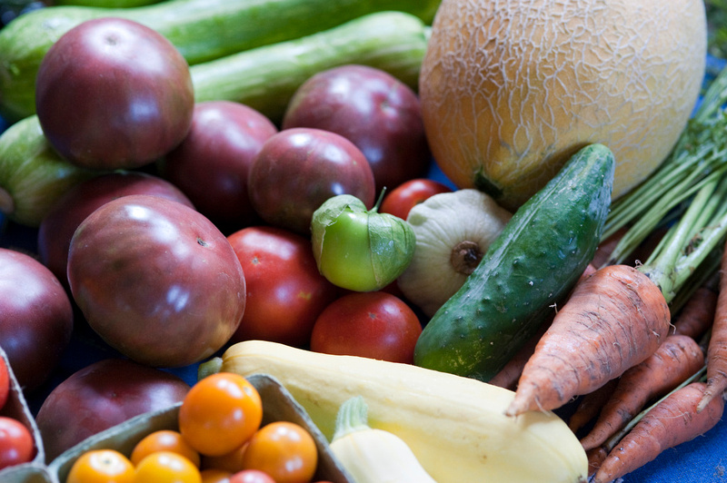 A photo of a collection of vegetables including potatoes, tomatoes, summer squash, carrots and a melon