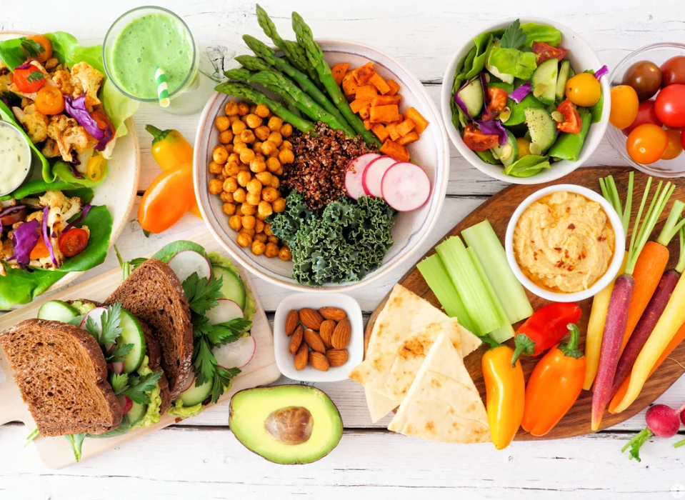 Table full of fresh foods including fruits, vegetables, and sandwiches. 