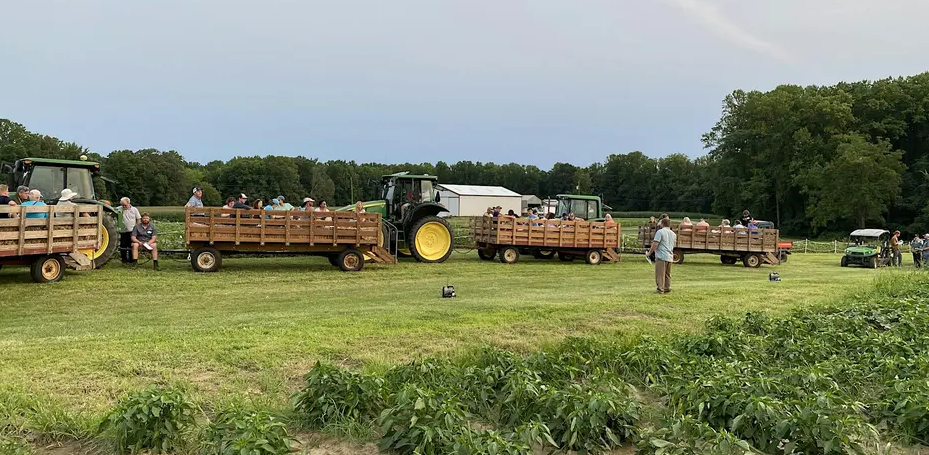 Presenting Speaker in field surrounded by tractors with wagons filled with spectators