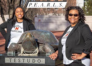 Two faculty members standing by a Testudo statue that has pearls on it