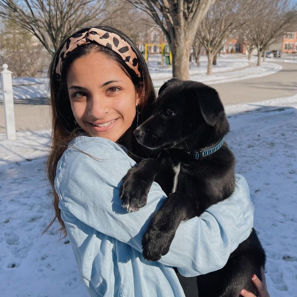 Jaanavi standing in the snow, smiling and holding a puppy