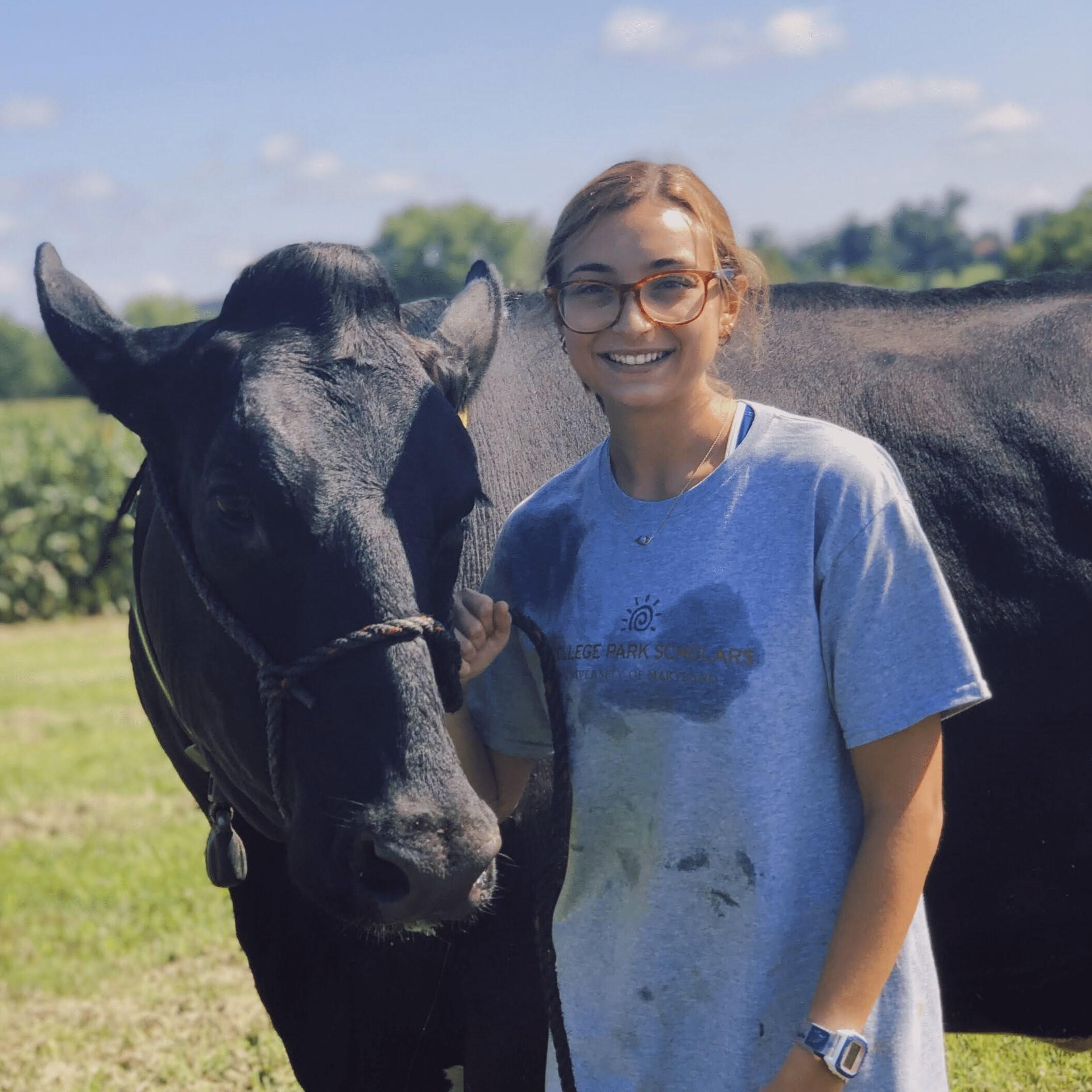 Shannen is smiling and posing next to a black angus cow