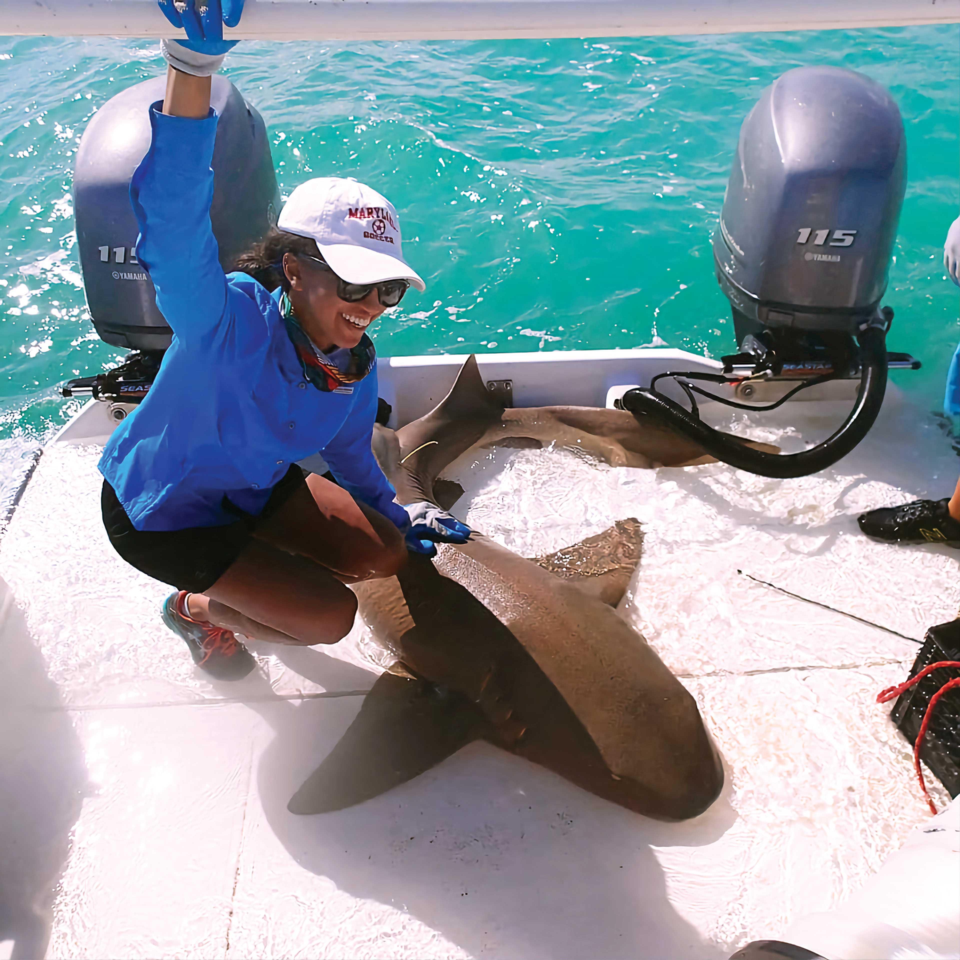 Samara Nehemiah posing with small shark on edge of boat. 