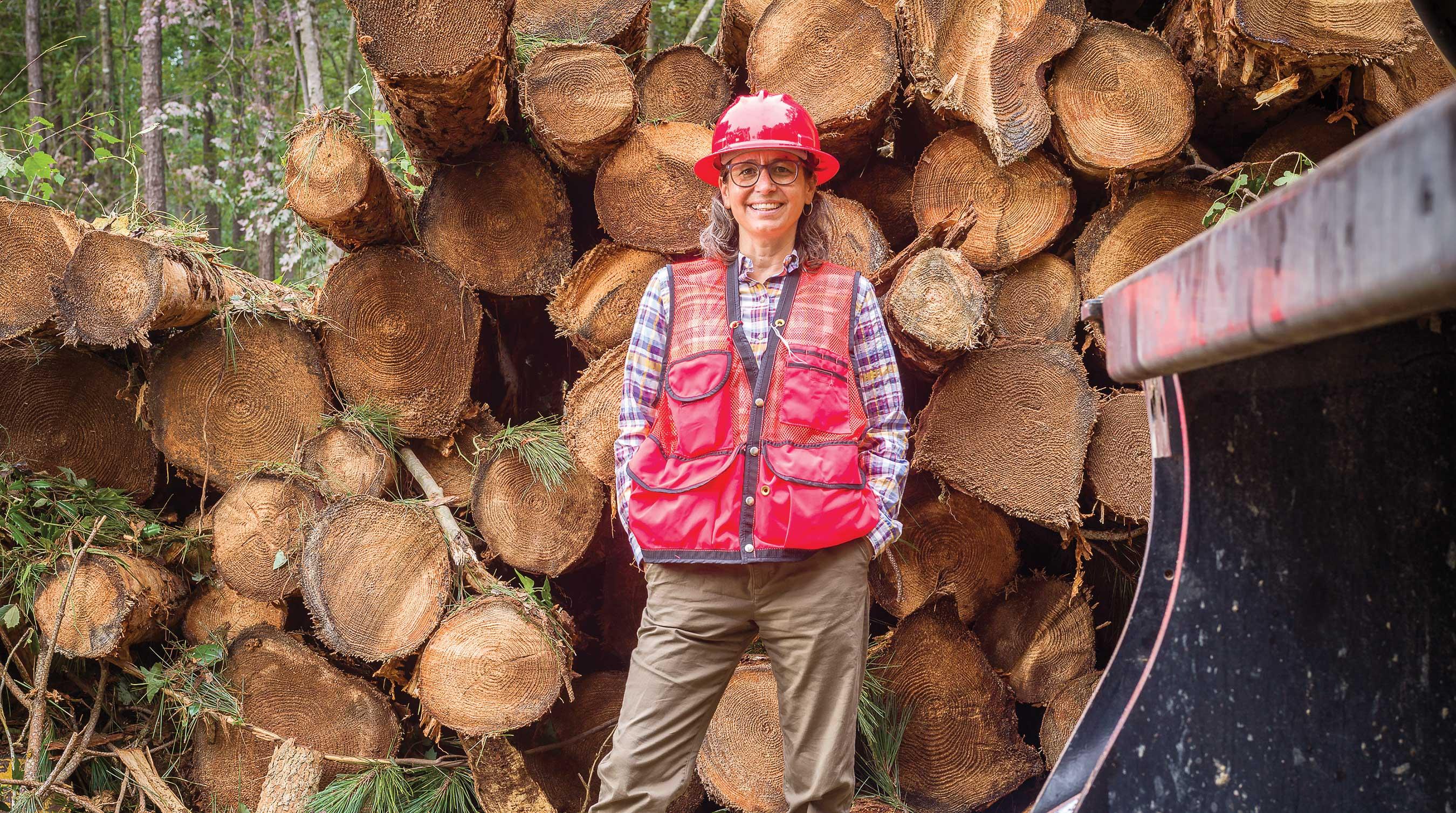 Forest Stewardship Educator Agnes Kedmenecz smiling while standing in front of chopped lumber. 