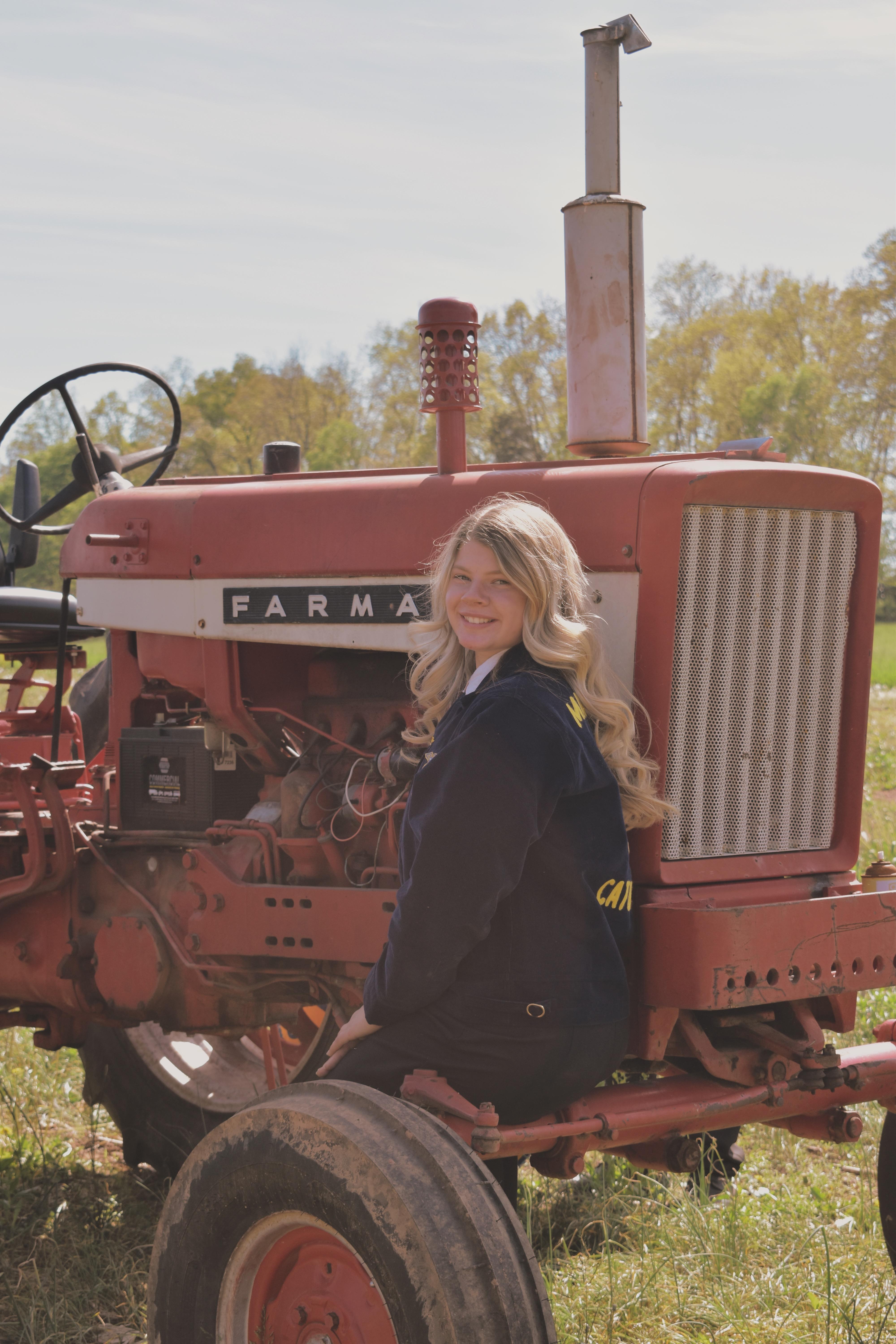 Cheyenne Van Echo. Happy student wearing an FFA jacket and posing with Farmall tractor.