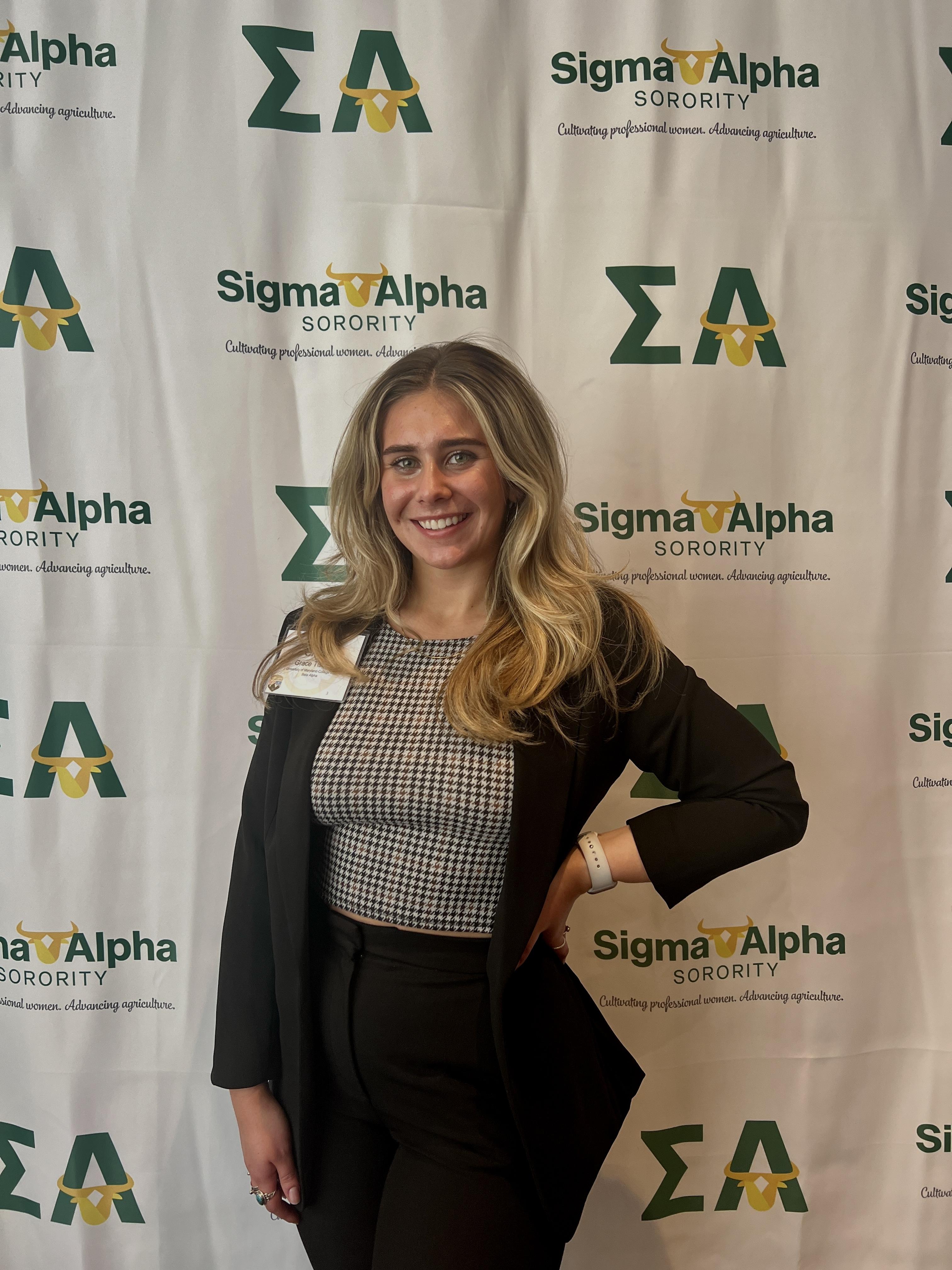 Grace Tisone. Happy student posing in front of Sigma Alpha backdrop. 