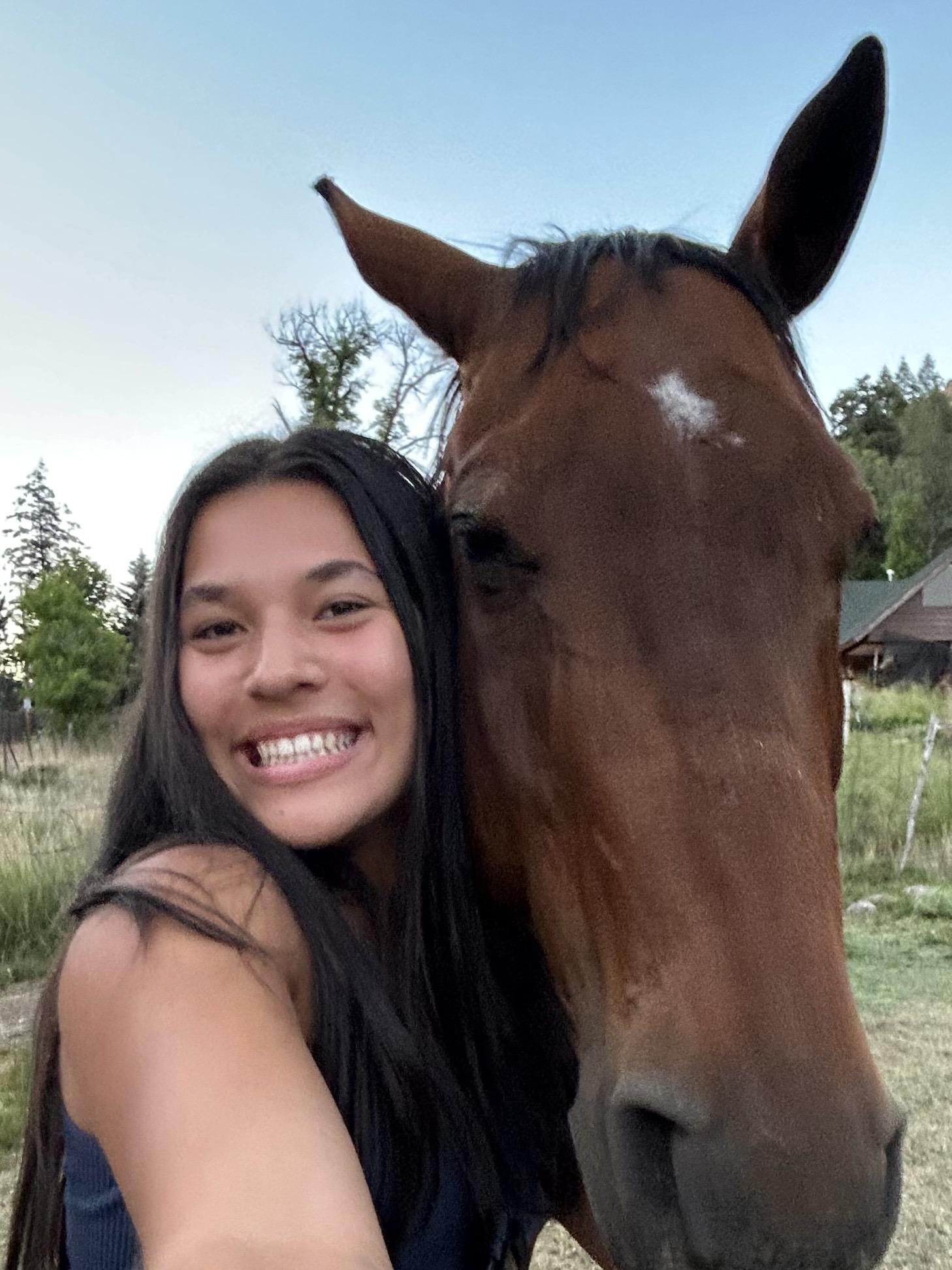 Lexi Urbanz. Joyful student standing eye level with a handsome brown horse.