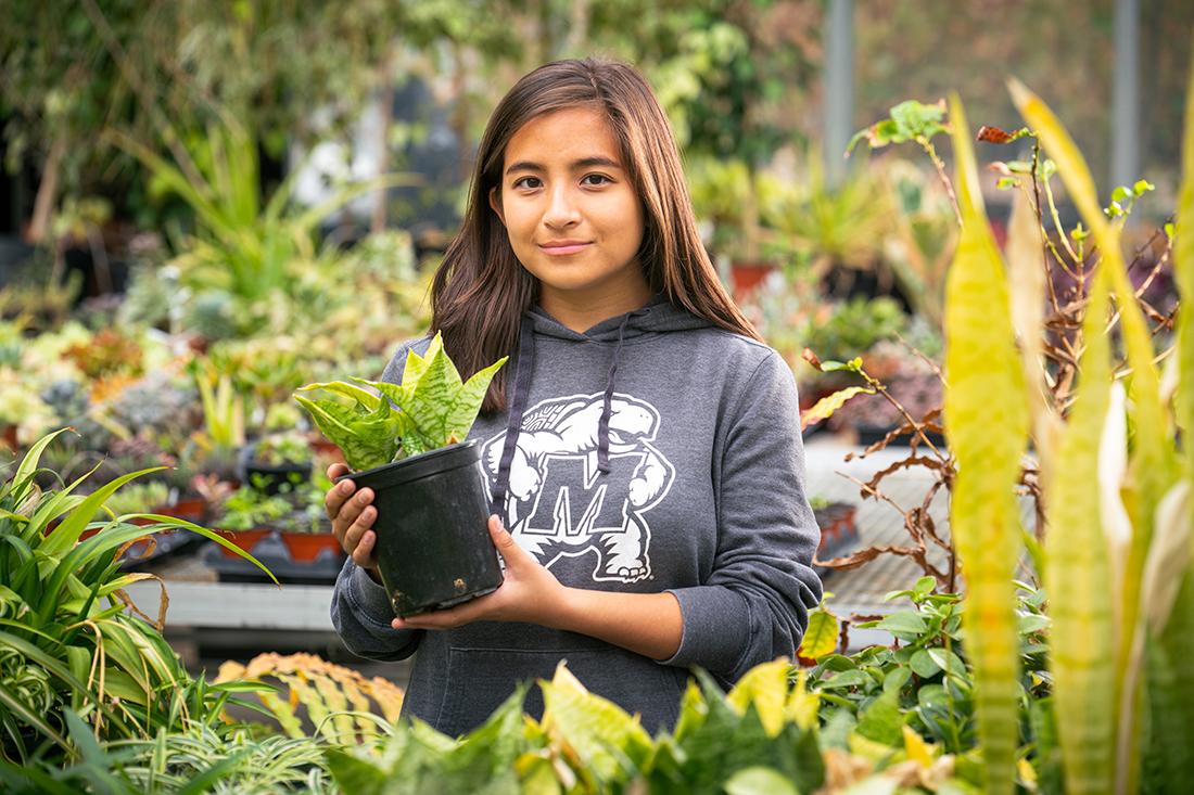 Student holding a plant in the greenhouse