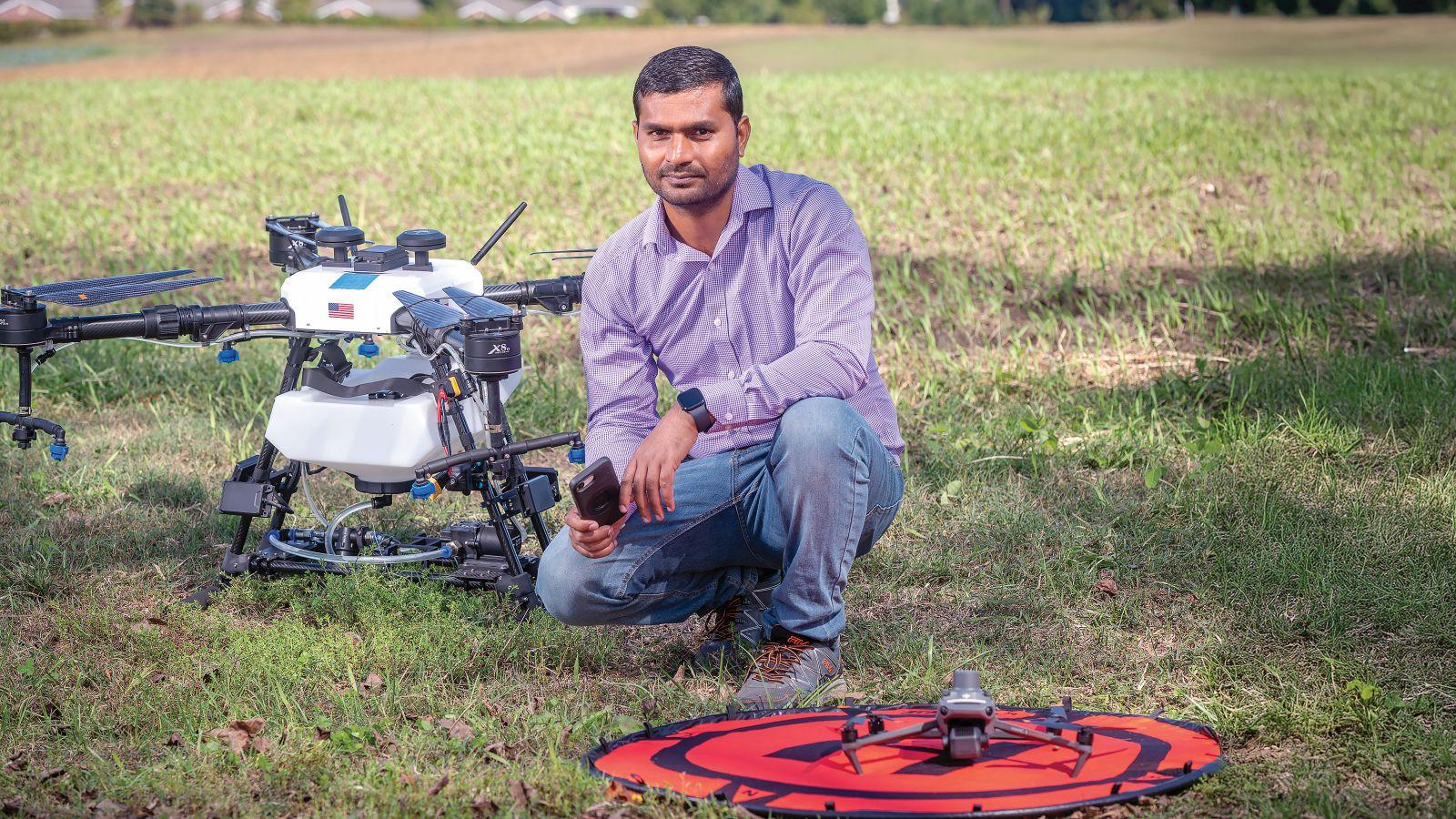 Hemendra Kumar sitting next to a drone at a farm