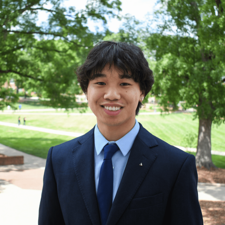 Kevin is wearing a suit and tie, smiling in front of McKeldin Mall