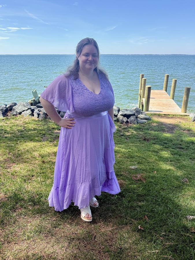 In a lavendar-colored flowing dress, a smiling student stands in front of the Chesapeake Bay watershed.