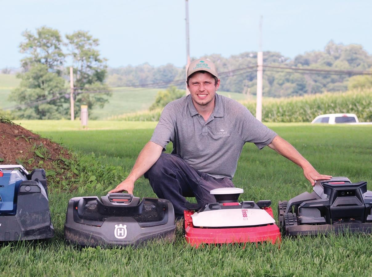 Alumn Brandon Writt kneeling over an autonomous mower 