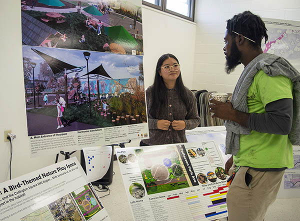 Student Grazelle Gray stands in front of her poster presenting her ideas to a community member.