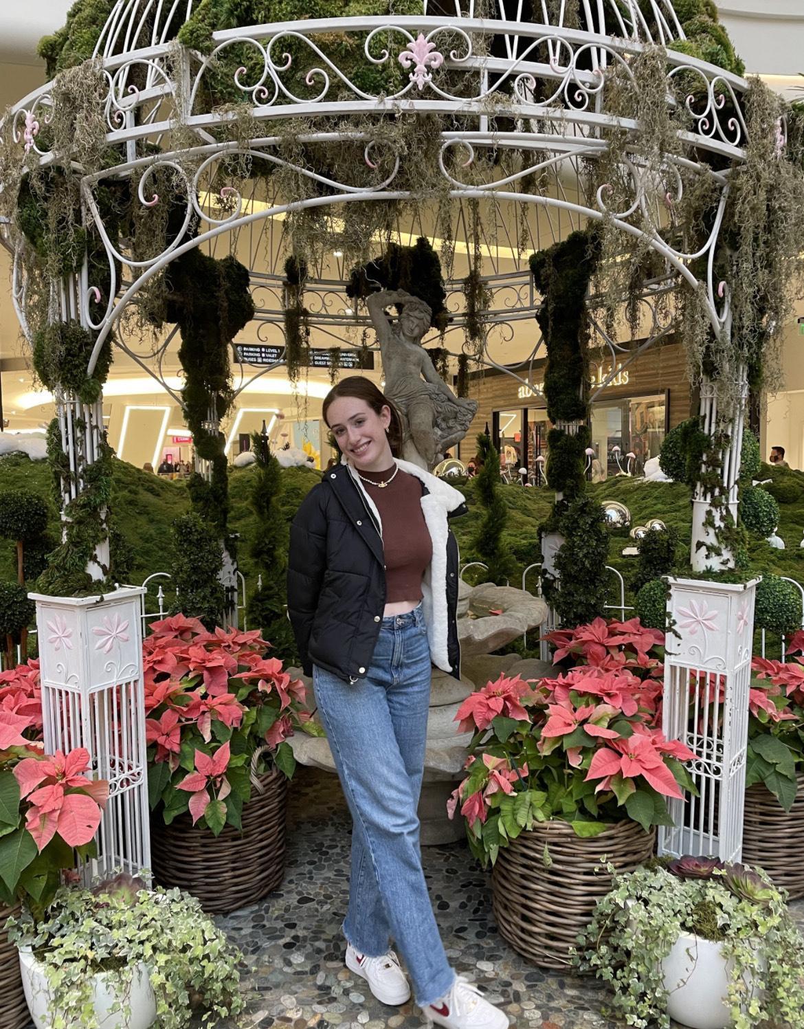 Natalie Cantagallo. Smiling student in forefront of pink flowers and a lovely gardenscape.